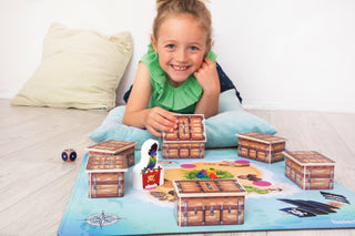 Kind spielt beleduc Piratenspiel mit Schatztruhen auf einer Spielmatte.