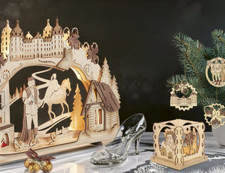 Holzdekor mit märchenhafter Szene: Schloss, Reiter, Hütte und gläserner Schuh erinnern an Aschenputtel. Ein kleiner Weihnachtsbaum ist mit ähnlichen Ornamenten geschmückt – kunstvoll und nostalgisch gestaltet.