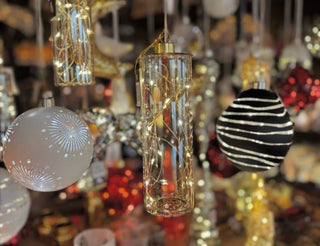 Weihnachtsdekorationen an einem Display: weiße Kugel mit Feuerwerksmuster, zylindrische Glasdeko mit Lichterkette und schwarze Kugel mit weißen Streifen. Im Hintergrund weitere bunte Deko-Elemente.