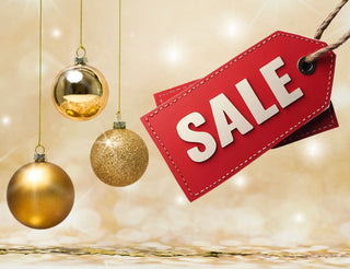 Drei goldene Weihnachtskugeln hängen vor einem glitzernden Hintergrund. Rechts sind zwei rote Preisschilder mit weißer Aufschrift „SALE“ zu sehen – ideal für weihnachtliche Verkaufsaktionen.