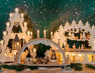 Beleuchteter Schwibbogen mit winterlicher Dorfszene: geschnitzte Häuser, Bäume, spielende Kinder und Schneemänner. Vor dunklem grünen Hintergrund mit Schneeflocken entsteht eine festliche Weihnachtsstimmung.