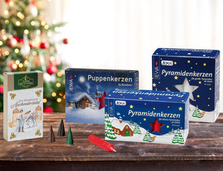 Weihnachtlich dekorierter Tisch mit Kerzen und Räucherwerk: Puppenkerzen, Pyramidenkerzen in zwei Größen und Räucherkerzen ‚Echt Erzgebirgischer Aschenbrödel‘ vor beleuchtetem Weihnachtsbaum.