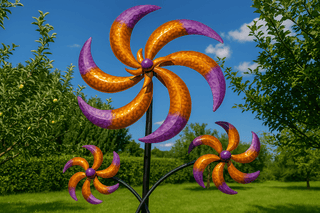 Drei bunte Windräder mit orange und lila Flügeln stehen im grünen Garten. Im Hintergrund sind Bäume, Gras und ein blauer Himmel mit wenigen Wolken zu sehen.