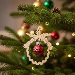 Christbaumschmuck mit roter Kugel (8,5 cm), dekorativ aufgehängt in einem filigranen Holzanhänger in Tannenzweig-Form am beleuchteten Weihnachtsbaum, umgeben von grünen Nadeln, Zapfen und warmen Lichtern.