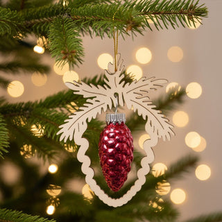 Christbaumschmuck Zapfen in Rot (8,5 cm), glänzender Glaszapfen in einem filigranen Holzornament am Tannenbaum hängend, umgeben von grünen Zweigen und warmen Weihnachtslichtern im Hintergrund.
