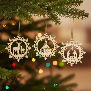 Christbaumschmuck „Klassisch“ im 3er Set aus Naturholz (8 cm), filigrane Sternornamente mit Motiven wie Reh, Kirche und Krippenszene, am Weihnachtsbaum aufgehängt, umgeben von grünen Tannenzweigen und warmen Lichterketten im Hintergrund.