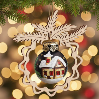 Christbaumschmuck „Stille Nacht“ (9 cm), farbig gestaltete Glaskugel mit winterlichem Hausmotiv, eingefasst in ein filigranes Holzornament mit Tannenmotiv, am Weihnachtsbaum hängend vor warm leuchtenden Lichtern im Hintergrund.