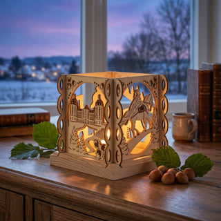 Kerzenhalter „Drei Haselnüsse für Aschenbrödel®“ für ein Teelicht (ca. 12 cm), aus naturbelassenem Holz mit einfarbig abgesetzten, filigranen Märchenmotiven wie Schloss, Kutsche und Reiter. Der warm leuchtende Kerzenhalter steht auf einem Holztisch vor einem Fenster mit winterlicher Landschaft im Hintergrund; daneben liegen Haselnüsse, Blätter und Bücher, die eine gemütliche, märchenhafte Atmosphäre schaffen.