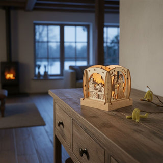 Kleiner Kerzenhalter aus naturfarbenem Holz für ein Teelicht mit Motiv „Drei Haselnüsse für Aschenbrödel®“ (2024), einfarbig abgesetzt. Der filigrane Mini‑Halter zeigt mehrere Märchenszenen mit Figuren, die durch das warme Kerzenlicht im Inneren sanft beleuchtet werden. Aufgestellt ist der Kerzenhalter auf einer Holzkommode; im Hintergrund sind ein Sessel, ein Kamin sowie ein Fenster mit winterlicher Landschaft zu sehen.