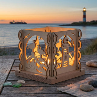 Natürlicher Holz-Kerzenhalter „Küstenliebe“ für ein Teelicht (ca. 12 cm), würfelförmig mit filigranen Küstenmotiven wie Möwen, Wellen und Leuchtturm. Der warm leuchtende Kerzenhalter steht auf einem Holztisch am Strand bei Sonnenuntergang; im Hintergrund sind das Meer, ein Leuchtturm und ein Schiff zu sehen. Auf dem Tisch liegen zudem Steine, Muscheln und ein Tuch im maritimen Stil.