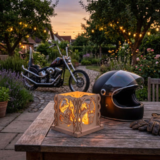 Natürlicher Holz-Kerzenhalter „Chopperfreund“ für ein Teelicht (ca. 12 cm), würfelförmig mit filigranen Motorrad-Motiven aus Holz. Der beleuchtete Kerzenhalter steht auf einem Holztisch im Garten bei Dämmerung; daneben befinden sich ein schwarzer Motorradhelm und Handschuhe. Im Hintergrund ist ein Chopper-Motorrad auf einem gepflasterten Weg sowie ein stimmungsvoll beleuchteter Garten mit Lichterkette zu sehen.