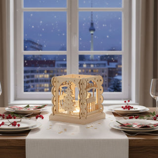 Kerzenhalter aus naturfarbenem Holz für ein Teelicht mit Motiv „Berlin“, mittig auf einem festlich gedeckten Tisch platziert. Der quadratische Halter zeigt filigrane Ausschnitte mit Berliner Wahrzeichen wie dem Brandenburger Tor, Fernsehturm und einem stilisierten Weihnachtsbaum, die vom warmen Kerzenlicht im Inneren beleuchtet werden. Rundherum stehen Teller, Gläser und rote Beeren als Dekoration; im Hintergrund ist durch ein Fenster eine winterliche Berliner Stadtszene mit Fernsehturm und fallendem Schnee