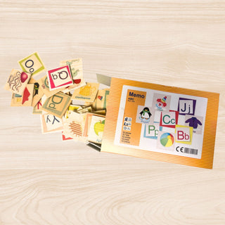 Offene Verpackung eines farbenfrohen ABC‑Memospiels auf einem hellen Holztisch; zahlreiche kleine Holzplättchen mit Buchstaben, Bildern und Wörtern liegen verstreut daneben, während auf der Verpackung Illustrationen wie ein Clown, ein Pinguin sowie Buchstabenpaare (z. B. Cc, Bb, Jj) abgebildet sind.