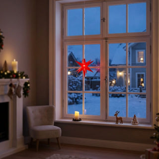 LED Adventsstern von HGD in Rot mit einem Durchmesser von 8 cm. Der kleine, batteriebetriebene Stern hängt vor einem großen Fenster und leuchtet in kräftigem Rot. Durch die Fensterscheiben ist eine verschneite Winterlandschaft mit beleuchteten Häusern zu sehen. Im gemütlich dekorierten Wohnraum befinden sich ein Sessel, ein Kamin mit weihnachtlichem Schmuck sowie dekorative Figuren und eine LED-Kerze auf der Fensterbank.