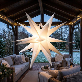 Weißer LED-Adventsstern für Außen von HGD mit 60 cm Durchmesser, aufgehängt unter einer überdachten Terrasse. Der große, mehrzackige Stern leuchtet in warmweißem Licht und bildet den Mittelpunkt einer gemütlichen Outdoor-Lounge. Umgeben von Sitzmöbeln mit Kissen und Decken, einer dezenten Lichterkette sowie einem winterlichen Garten mit leicht verschneiter Rasenfläche sorgt der festliche Adventsstern für eine stimmungsvolle Weihnachtsatmosphäre im Außenbereich.