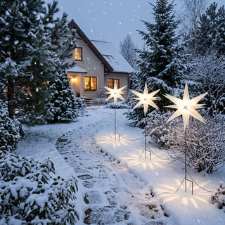 LED-Adventsstern 3er Set mit Bodenspießen von HGD in Weiß mit 35 cm Durchmesser. Drei leuchtende Weihnachtssterne sind entlang eines verschneiten Gartenwegs platziert und sorgen für eine stimmungsvolle Beleuchtung im Außenbereich. Die Sterne strahlen warmweißes Licht aus und werden mithilfe von Bodenspießen sicher im Schnee befestigt. Im Hintergrund sind ein winterlicher Garten mit schneebedeckten Tannen sowie ein beleuchtetes Wohnhaus zu sehen, die gemeinsam eine festliche Advents- und Weihnachtsatmosphäre