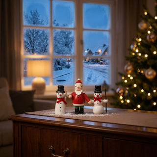Miniatur „Weihnachtsmann mit Schneemännern“, 3er Set (ca. 5 cm), farbig gestaltet mit einem Weihnachtsmann in roter Kleidung zwischen zwei Schneemännern mit Hüten und Schal. Die Figuren stehen auf einem Möbelstück in einer gemütlichen Wohnstube; im Hintergrund ein Fenster mit verschneiter Winterlandschaft sowie ein geschmückter Weihnachtsbaum und warme Beleuchtung, die eine festliche Atmosphäre schaffen.