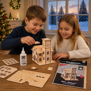 Bastelsatz „Rathaus“ aus naturbelassenem Holz mit einer Höhe von 10,5 cm. Auf einem Holztisch bauen zwei Kinder ein detailreiches Rathausmodell zusammen. Das teilweise montierte Holzgebäude mit Uhrturm steht in der Mitte, umgeben von vorgestanzten Holzteilen und einer Flasche Holzleim. Rechts liegt die Verpackung des Bastelsets mit der Abbildung des fertigen Rathauses. 