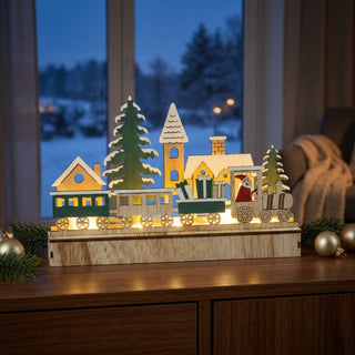 LED-Diorama „Weihnachtseisenbahn“, ca. 15 cm groß, aus Holz gefertigt, mit detailreicher Szene eines beleuchteten Zuges mit mehreren Waggons, Weihnachtsmann-Figur, Tannenbäumen und Häusern, warmweiß hinterleuchtet und dekorativ auf einer Kommode platziert.