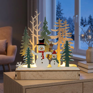 LED-Diorama „Schneemann“, ca. 15 cm groß, farbig gestaltet, mit zwei Schneemännern in winterlicher Waldszene mit Tannenbäumen, warmweiß beleuchtet und mit integrierter Timerfunktion, dekorativ auf einem Tisch platziert.