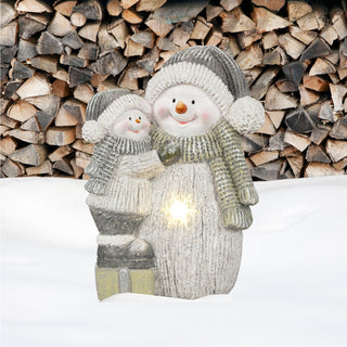 **Alt-Text:**  
XL Schneemann mit Schneemannkind als Winter‑Dekofigur aus Magnesia, beide mit gestrickten Mützen, Schals und Handschuhen, integrierte warm leuchtende LED‑Schneeflocke im Körper des großen Schneemanns, stehend im Schnee vor einem Hintergrund aus gestapelten Holzscheiten, geeignet für stimmungsvolle Weihnachtsdekoration im Außenbereich.
