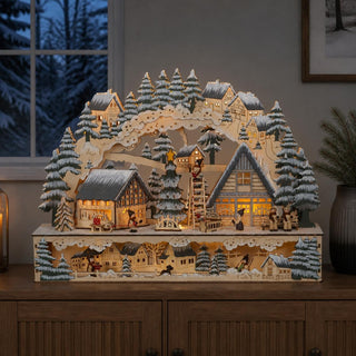 LED-Lichterbogen „Weihnachtsbaum“ mit verschneiten Häusern, Tannenbäumen und beleuchtetem Weihnachtsbaum in einer detailreichen Winterlandschaft auf einem Sideboard.