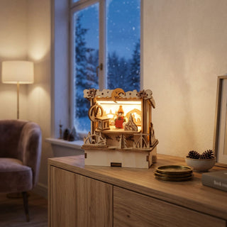 LED-Weihnachtsmarkthütte „Holzwaren“ (11 cm), naturfarbene Holzszene mit Verkäuferfigur und dekorativen Handarbeiten, warm beleuchtet auf einer Kommode vor winterlicher Fensterkulisse platziert.