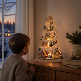 LED-Lichterspitze „Wichtelweihnacht“ aus naturfarbenem Holz mit warmweißer Beleuchtung auf einer Kommode in einem festlich dekorierten Wohnraum. Die baumförmige Weihnachtsdekoration zeigt auf mehreren Ebenen kleine Häuser, verschneite Tannen, Rehe, einen Wichtel mit Geschenken und weitere winterliche Details. Ein filigraner Stern krönt die Spitze der 48 cm hohen Lichterdekoration. 