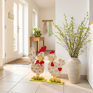 Dekofiguren Hühner (2er-Set, ca. 30 cm), zwei große Holz-Hühner in naturfarbenem Look mit roten Details und gelben Füßen. Stehen auf dem Boden im Eingangsbereich neben einer Vase mit Zweigen, im Hintergrund helle Wohnräume und Blick zur Eingangstür.