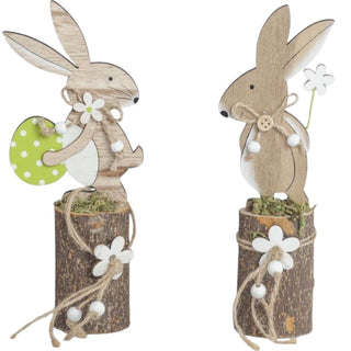 Osterhasenpaar auf Baumstamm (ca. 20 cm), zwei naturfarbene Holzhasen auf kleinen Baumstämmen mit Moos, verziert mit Blüten, Kordel und Osterei; freigestellt vor hellem Hintergrund.