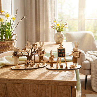 Osterhasen auf Sockel (2er-Set, ca. 13 cm), naturfarbene Holzfiguren mit zwei Szenen: Hase am Baum mit Vogelmotiv und Hasenschule mit Tafel. Platziert auf einer Kommode mit Frühlingsdeko vor einem hellen Fenster.