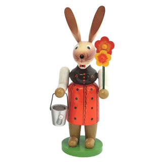 Farbige Osterhäsin aus Holz mit Gießkanne und Blumen in der Hand.