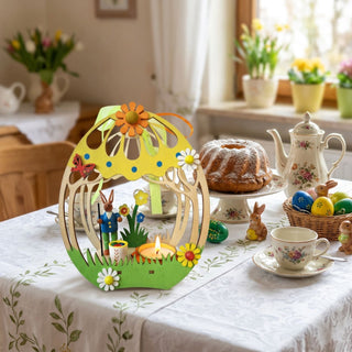 Kerzenhalter für Teelicht „Ei mit Hase“ (ca. 17 cm), farbig gestaltetes Deko-Ei mit Hasenfigur, Blumen und brennendem Teelicht. Arrangiert auf einem gedeckten Tisch mit Kuchen, Geschirr und bunten Ostereiern, vor einem Fenster mit Frühlingsblumen im Hintergrund.