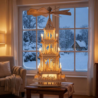 XXL-Weihnachtspyramide „Wald“ aus naturbelassenem Holz, ca. 100 cm hoch, elektrisch betrieben und ohne Bestückung, mit mehreren Etagen und filigranen Waldmotiven sowie Flügelrad. Warm beleuchtet auf einem Tisch vor einem großen Fenster mit verschneiter Winterlandschaft im Hintergrund.