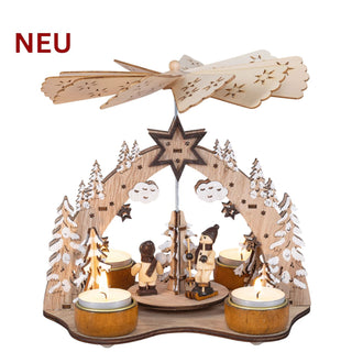 Weihnachtspyramide „Winterfreuden“ aus naturfarbenem Holz für vier Teelichter. Die filigrane Winterlandschaft zeigt verschneite Tannenbäume, Sterne und zwei handbemalte Figuren bei winterlichen Freizeitaktivitäten auf einer drehbaren Plattform. Die Wärme der vier Teelichter setzt das große Flügelrad in Bewegung und lässt die Szene rotieren. Mit ihren liebevollen Details und der Höhe von 21 cm sorgt die Weihnachtspyramide für eine stimmungsvolle Advents- und Weihnachtsdekoration.