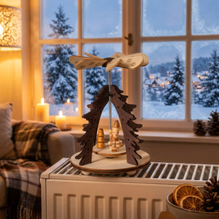 Weihnachtspyramide „Wärmespiel Weihnachtsmann“ aus naturbelassenem Holz (12 cm) mit Flügelrad. Kleine Szene mit Weihnachtsmann und Tannenbaum, die durch aufsteigende Wärme in Bewegung gesetzt wird. Auf einer Fensterbank vor verschneiter Winterlandschaft, warm beleuchtet und dekoriert.
