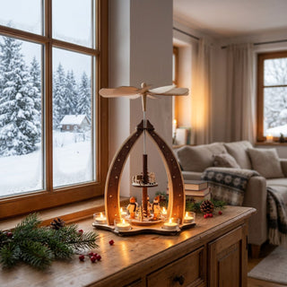 Weihnachtspyramide „Winterkinder“ aus naturbelassenem Holz (37 cm) mit sechs Teelichtern und Flügelrad. Offene Bogenform mit Winterkind-Figuren um einen Baum. Auf einer Kommode vor verschneitem Fenster, in gemütlicher Wohnatmosphäre dekoriert.