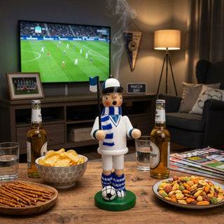 Räuchermännchen „Fußballer“ in Weiß/Blau (23 cm) mit Ball und Fahne, rauchend auf Tisch vor laufendem Fußballspiel im TV.