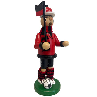 Räuchermännchen „Fußballer“ aus Holz, ca. 23 cm groß, in dunkelroter Farbgestaltung aus schräger Seitenansicht. Die Figur steht auf einem runden grünen Sockel neben einem schwarz-weißen Fußball, trägt ein dunkelrotes Outfit mit schwarzen Details sowie einen rot-schwarz gestreiften Schal und passende gestrickte Beinwärmer und hält eine rot-schwarze Fahne an einem schwarzen Stab.