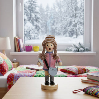 Farbiges Räuchermännchen „Mädchen mit Handy und Handtasche“ (20 cm) aus Holz. Die Figur trägt eine rosa Winterjacke, eine gestreifte Strickmütze, geflochtene Zöpfe und hohe Stiefel. In der einen Hand hält sie ein Smartphone, über der Schulter hängt eine helle Handtasche. Aus dem geöffneten Mund steigt Rauch auf. Das Räuchermännchen steht auf einem Tisch in einem gemütlichen Kinderzimmer mit buntem Bett, Büchern und einem großen Fenster, vor dem eine verschneite Winterlandschaft zu sehen ist.
