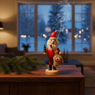 Farbiges Räuchermännchen „Weihnachtsmann“ (19 cm) aus Holz mit roter Kleidung, weißem Bart, kleinem Tannenbaum und Geschenkesack. Aus der Pfeife steigt feiner Rauch auf. Die Figur steht auf einem Holzmöbel neben Tannenzweigen. Im Hintergrund sind ein großes Fenster mit winterlicher Abendstimmung und warme Lichter zu sehen, die eine gemütliche Weihnachtsatmosphäre schaffen.