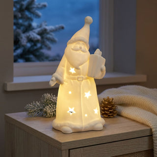 LED Weihnachtsmann „Geschenk“ (15 cm) in Weiß, warmweiß beleuchtet, mit ausgestanzten Sternmotiven und Geschenk in der Hand, als stimmungsvolle Tisch- oder Fensterdekoration in gemütlicher Winteratmosphäre.