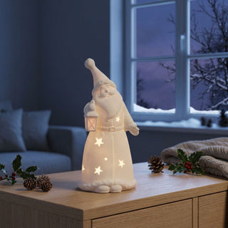 LED Weihnachtsmann „Laterne“ (15 cm) in Weiß, warmweiß beleuchtet, mit integrierter Laterne und ausgestanzten Sternmotiven, als stimmungsvolle Tisch- oder Fensterdekoration in gemütlicher Winterlandschaft.