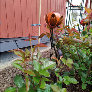 Solarbetriebener Gartenstecker in Blumenform mit orangefarbener Glaskugel und dekorativen Metallblättern im Rosenbeet.