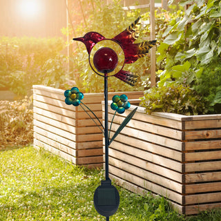 LED Solar‑Gartenstecker „Vogel“ in Rot aus Metall und Glas mit integrierter roter LED‑Glaskugel und dekorativen Blumenapplikationen, solarbetrieben, im Garten vor Holz‑Hochbeeten bei Sonnenschein platziert.