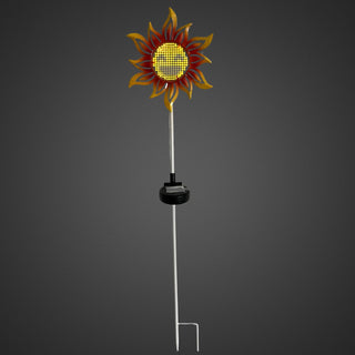 Gartenstecker „Sonnenblume“ mit gelb‑orangenen Blütenblättern, leuchtender Solar‑LED in der Mitte und Smiley‑Gesicht, auf Metallstab vor dunklem Hintergrund.