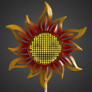 Nahaufnahme eines Gartensteckers „Sonnenblume“ mit gelb‑orangenen Blütenblättern und leuchtender Solar‑LED im runden Smiley‑Gesicht, vor dunklem Hintergrund.