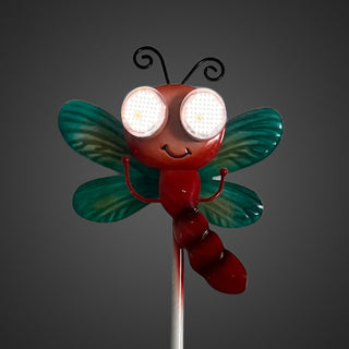 Gartenstecker „Libelle“ in Nahaufnahme mit grün schimmernden Flügeln, rotem Körper und leuchtenden Solar‑LED‑Augen mit wechselnder Blickrichtung, 77 cm hoch, vor dunklem Hintergrund.