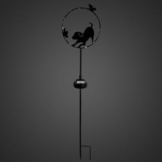 Gartenstecker aus schwarzem Metall mit spielender Hunde‑Silhouette in einem runden Rahmen. Der Hund ist in Bewegung dargestellt, begleitet von kleinen Schmetterlingsmotiven am Rand des Kreises. Ein integrierter Solar‑LED‑Lichtdraht beleuchtet den Rahmen dezent mit warmweißem Licht. Am Metallstab befindet sich das Solar‑Modul. Gesamthöhe 84 cm, freistehend vor dunklem Hintergrund.