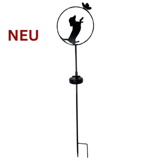 Gartenstecker aus schwarzem Metall mit stehender Hunde‑Silhouette in einem runden Rahmen. Der Hund richtet sich auf den Hinterbeinen auf und greift nach einem kleinen Schmetterling am oberen Rand des Kreises. Am Metallstab ist ein integriertes Solar‑LED‑Modul angebracht. Zum Einstecken in den Gartenboden